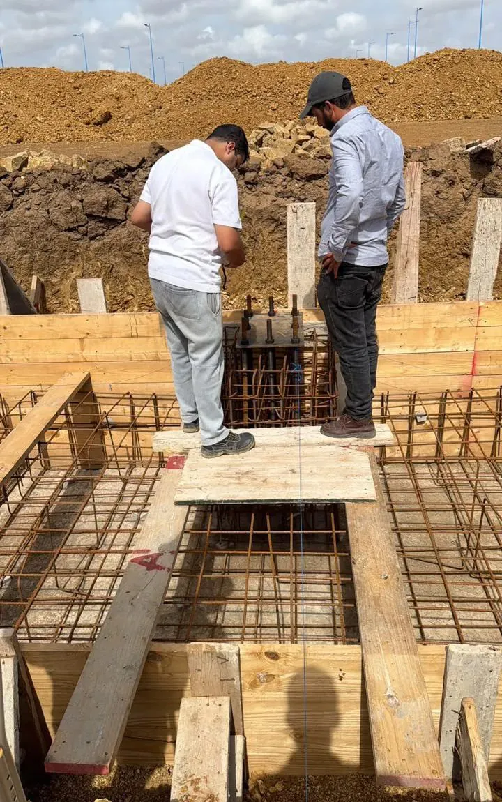 Deux personnes contrôlent le ferraillage d'une semelle sur un chantier